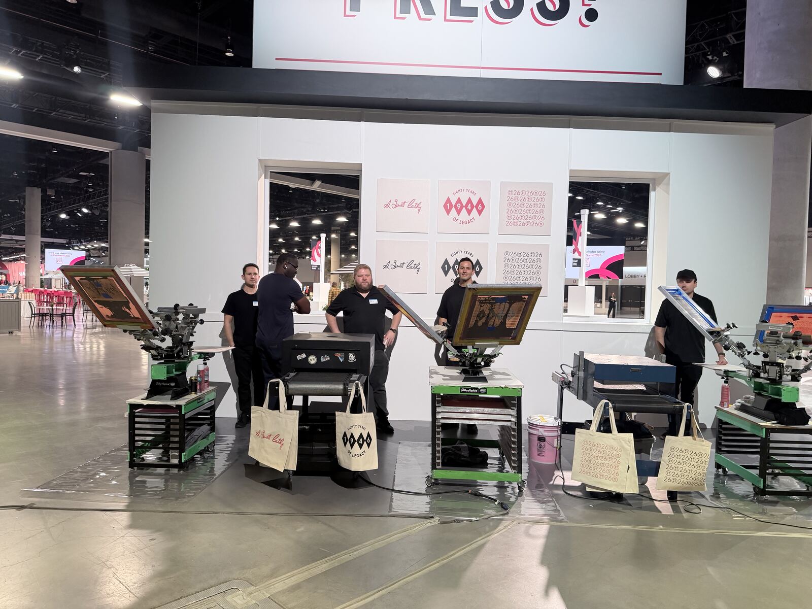 Embroidery and hat personalization equipment on display with decorated totes and apparel samples hung overhead