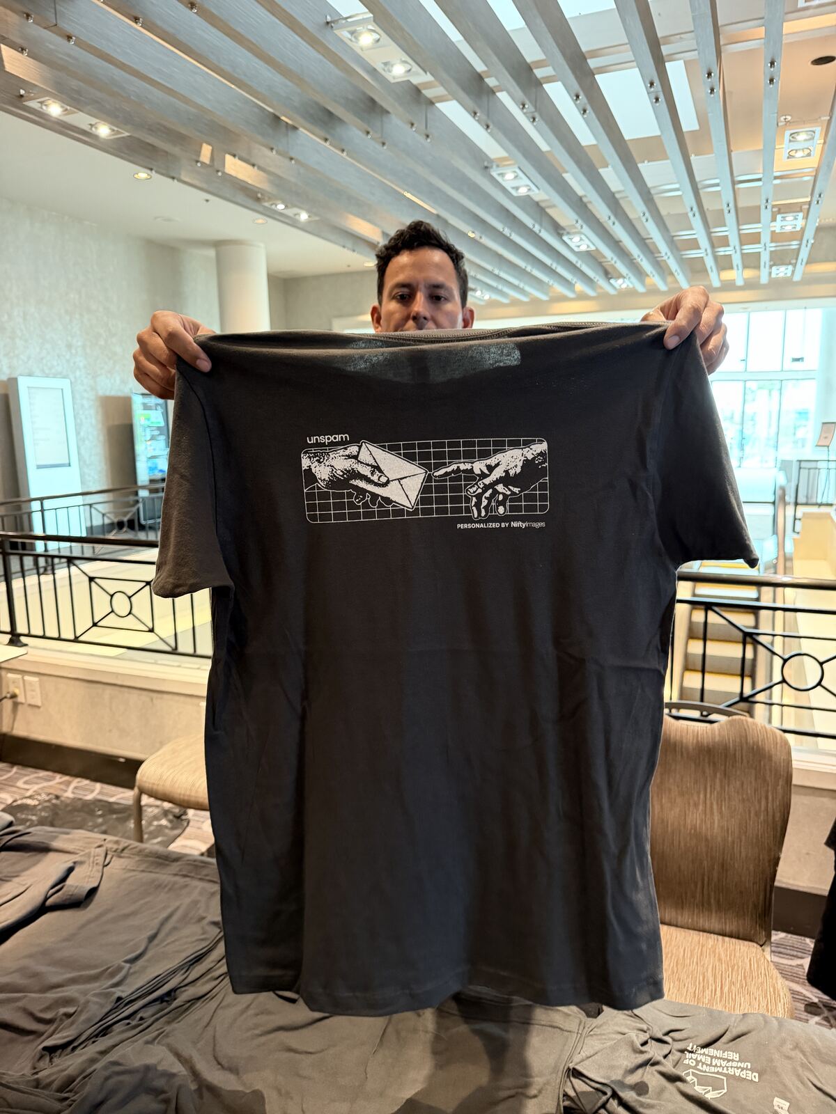 Person holding up a black screen-printed t-shirt with a minimalist graphic design